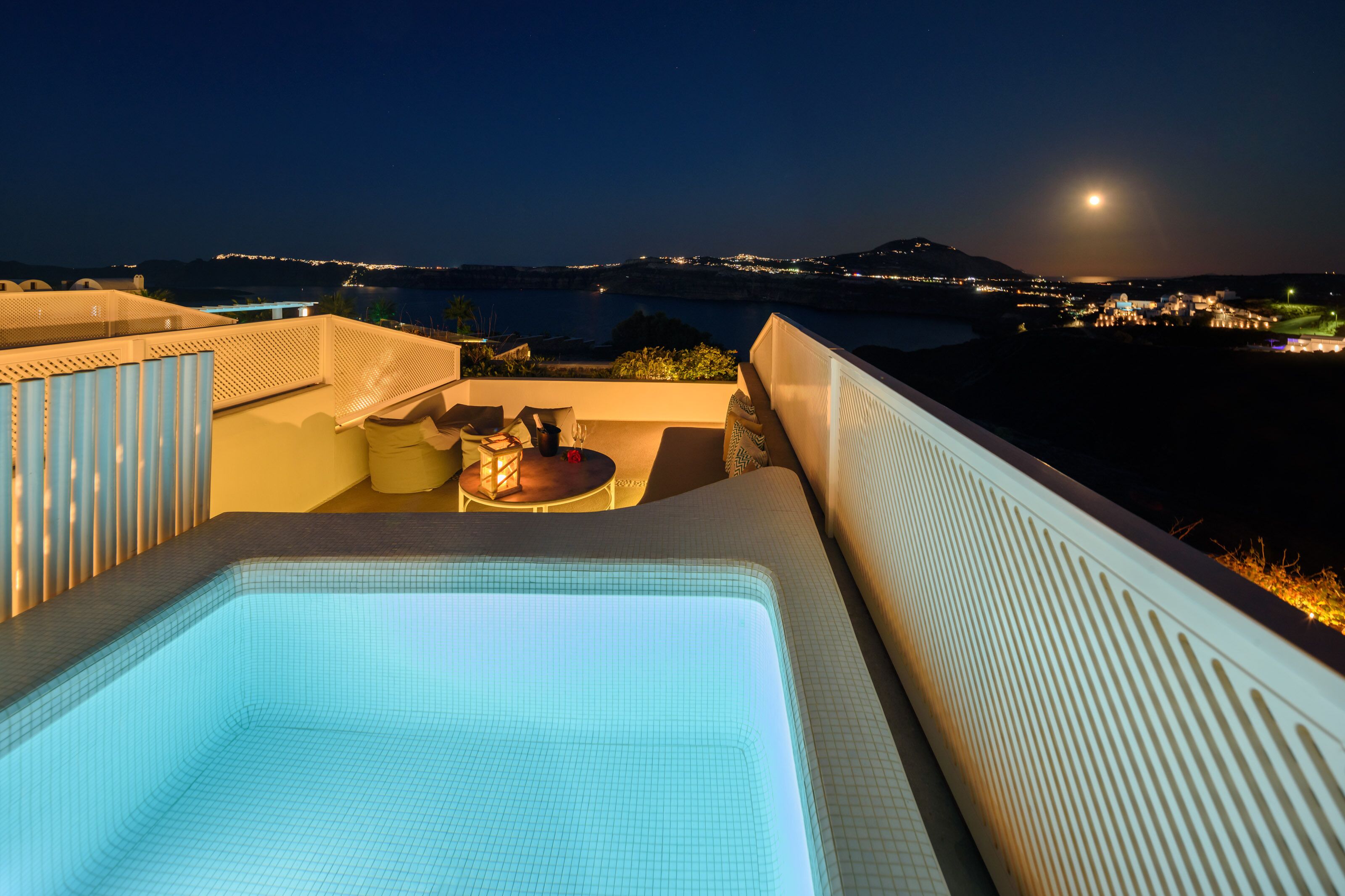 A rooftop pool area with a view of the sea and a moonlit night sky.