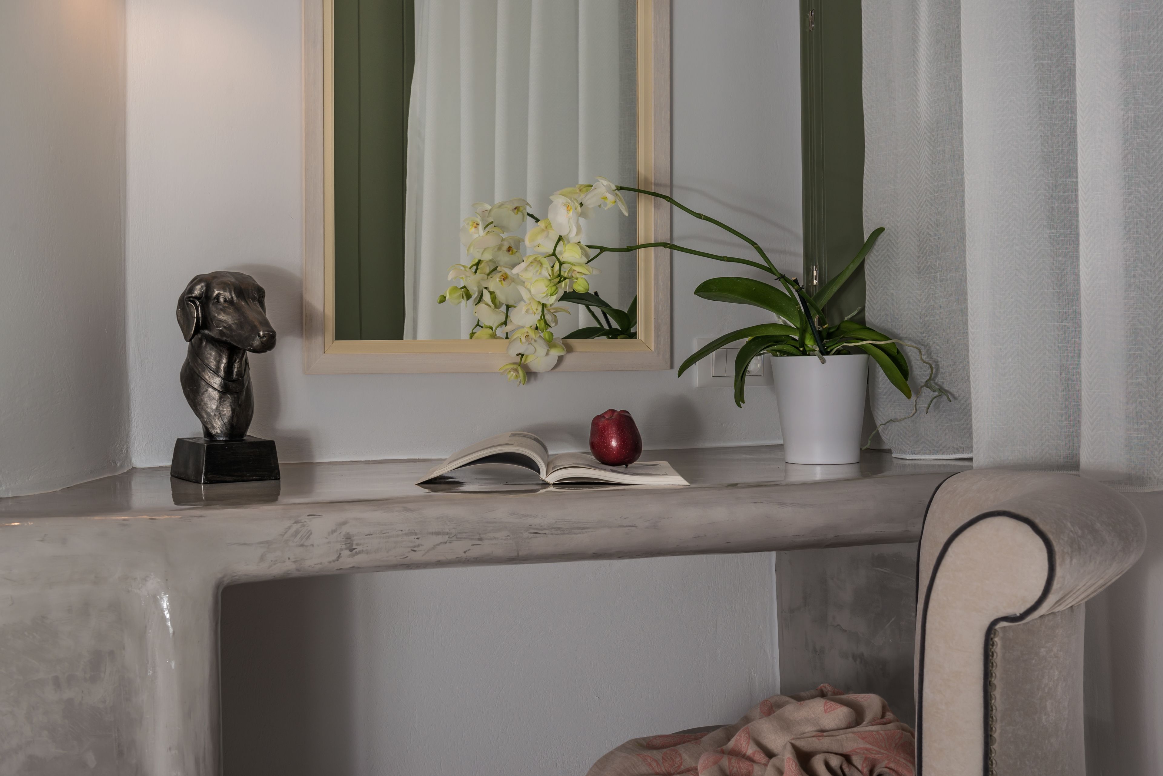 A marble console table with a statue, an open book, a red apple, white orchids, and a potted plant.