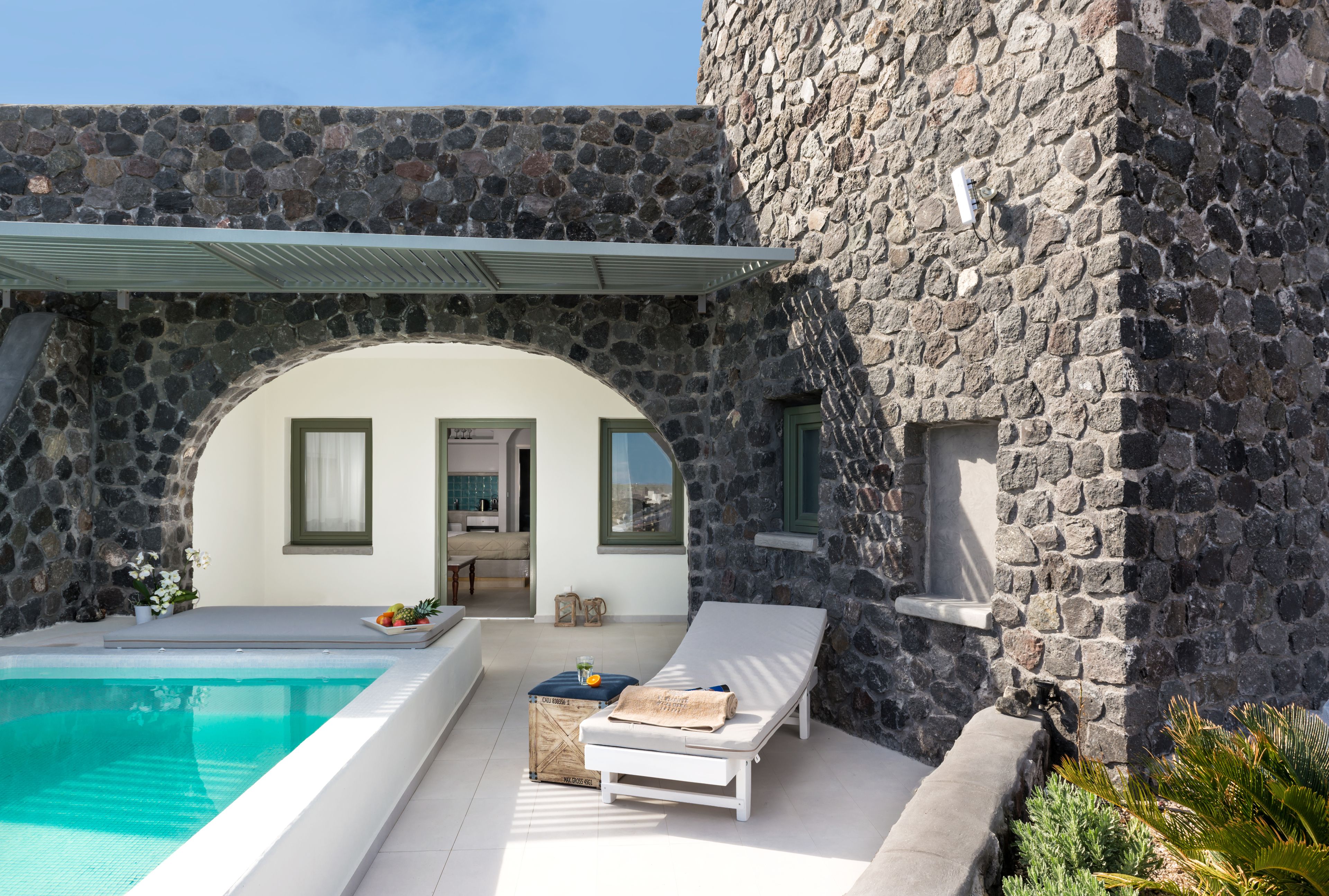 A stone building with a pool, a lounge chair, and a small table with a drink.