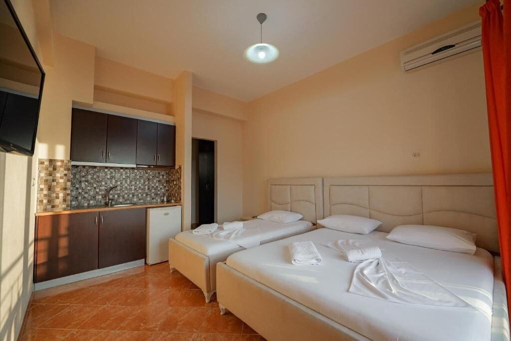 A hotel room with two beds, a kitchenette, and a bathroom.