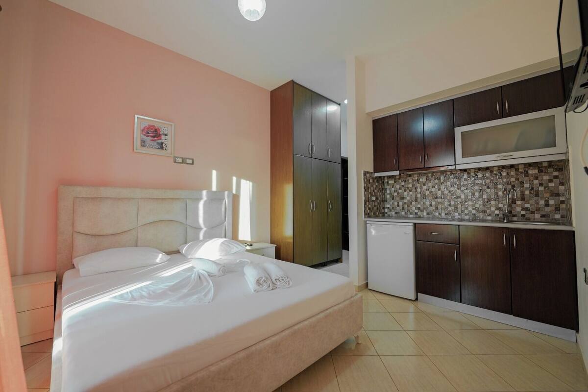 A bedroom with a bed, a nightstand, a wardrobe, a kitchenette with a microwave, and a tiled backsplash.