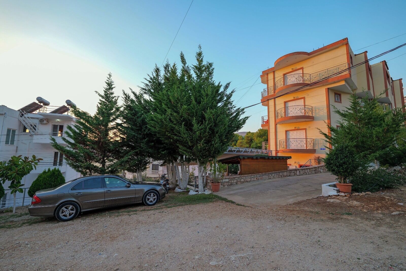 A residential building with a multi-story structure, a car parked in front, and surrounding greenery.