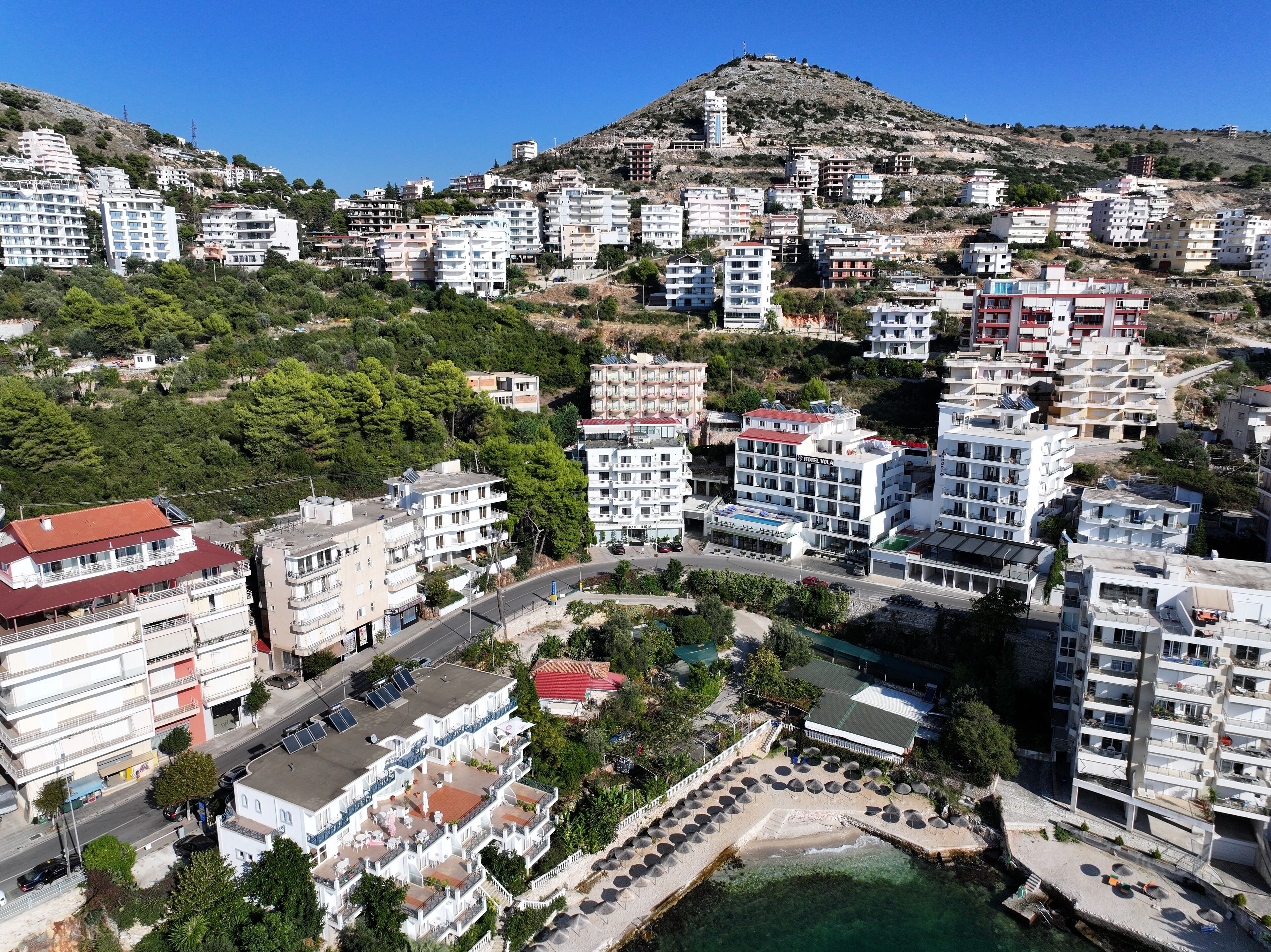 A coastal hotel with multiple floors, a swimming pool, and a view of the sea.