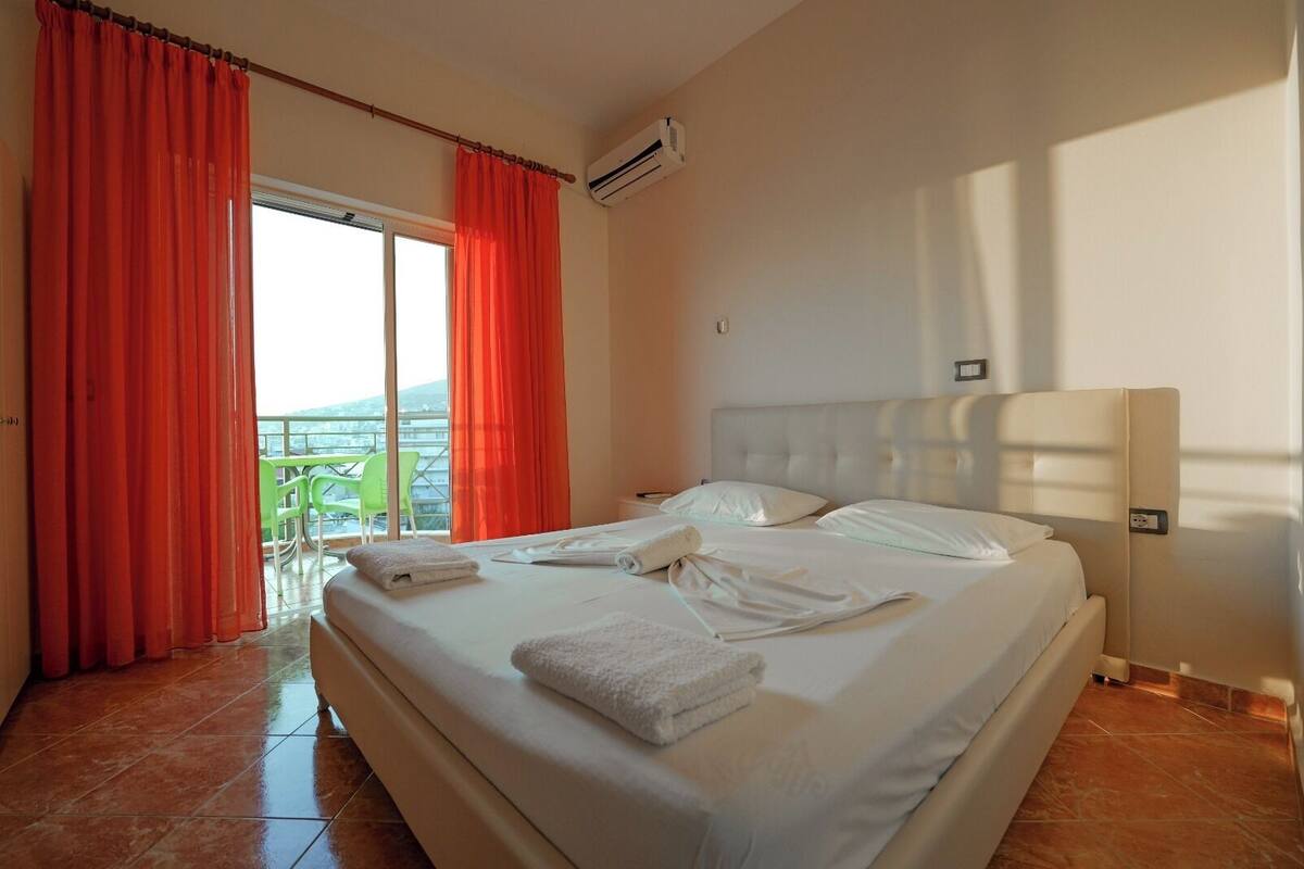 A hotel room with a large bed, a balcony with red curtains, and a view of the sea.