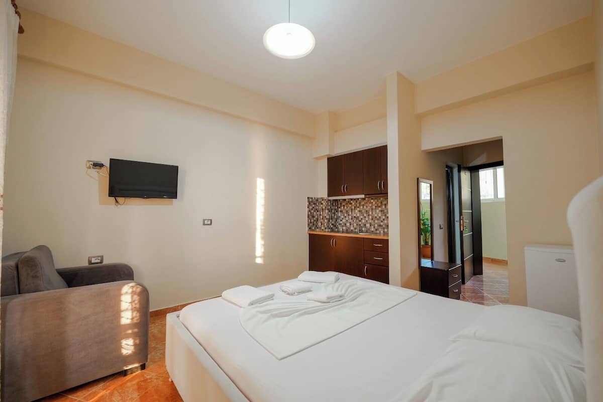 A hotel room with a bed, a TV mounted on the wall, a kitchenette, and a door leading to another room.
