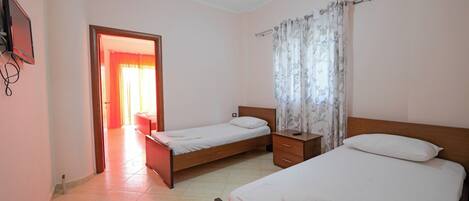 A hotel room with two single beds, a wooden nightstand, a small drawer, a TV mounted on the wall, and a bathroom visible through an open door.