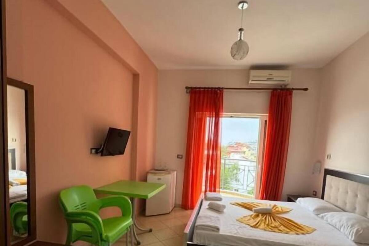 A hotel room with a bed, a desk with a chair, a television, and a window with red curtains.