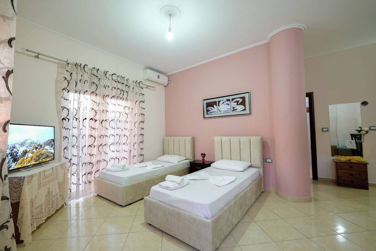 A hotel room with two beds, a TV, a painting, and a mirror.