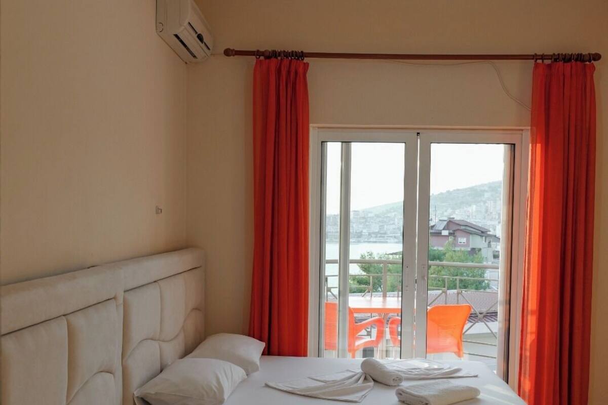 A hotel room with two beds, a ceiling fan, and a view of the city through large windows.