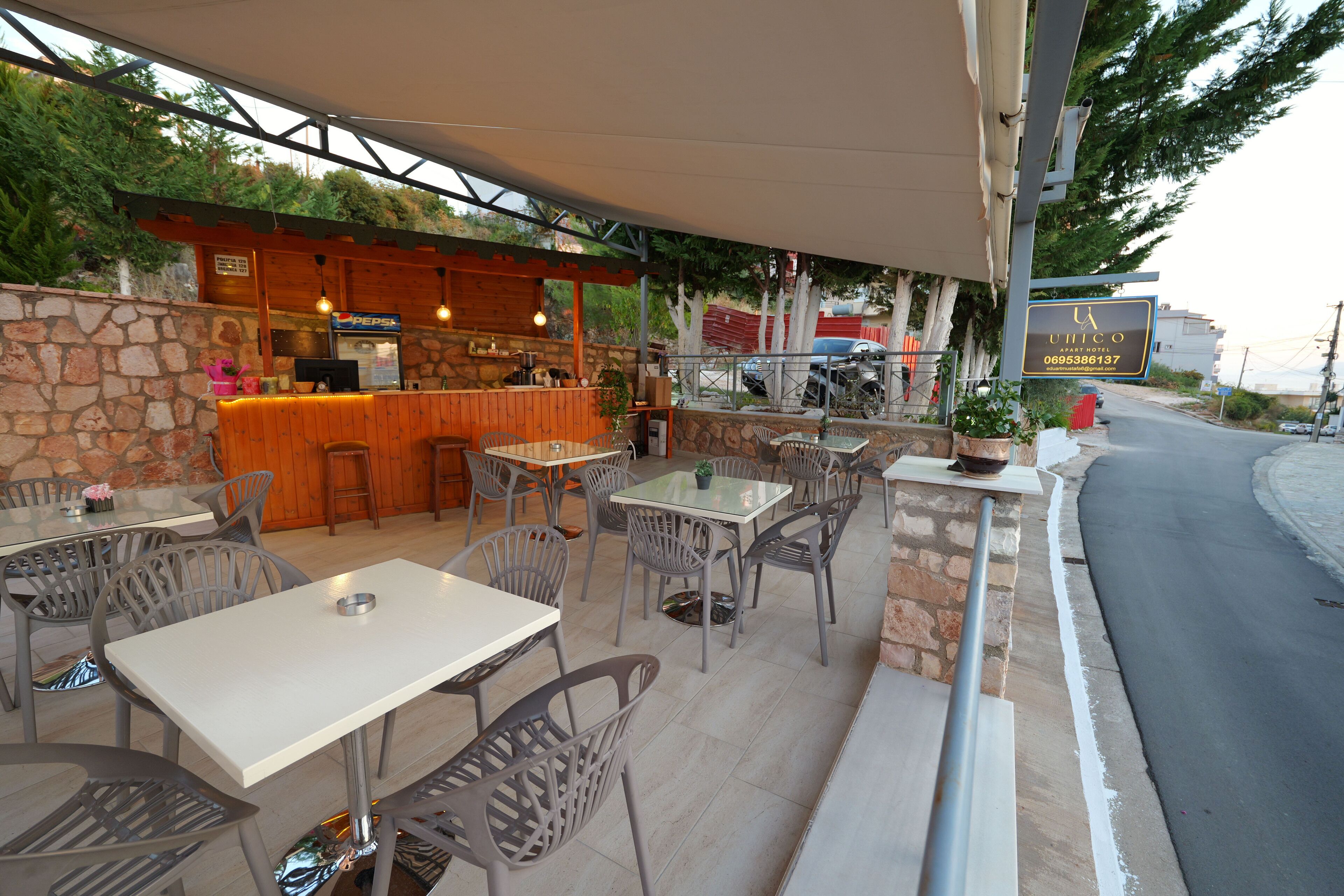 An outdoor cafe with tables and chairs, a bar area, and a stone wall.