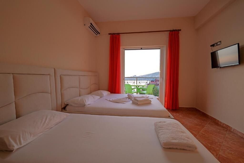 A hotel room with two beds, a TV, and a window with red curtains.