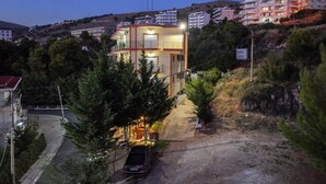 Edificio de dos pisos con balcón, rodeado de árboles y un coche estacionado.