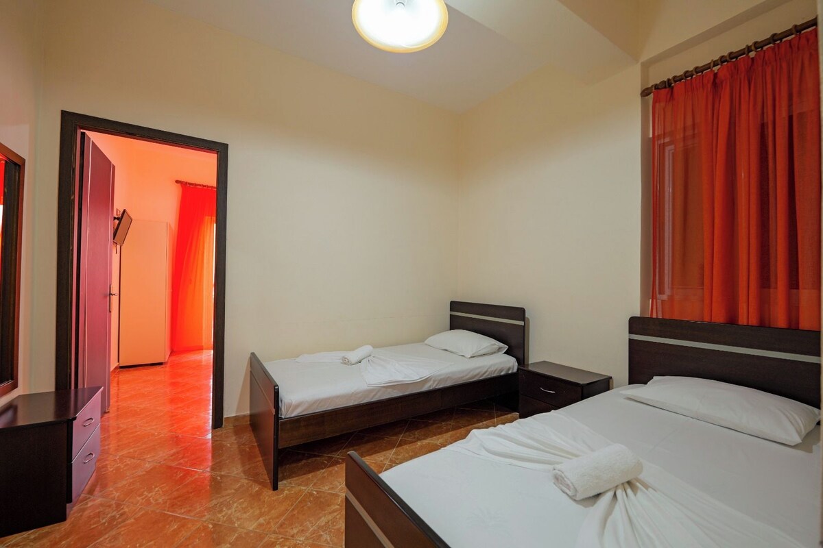 A hotel room with two beds, a small bedside table, a wardrobe, and a bathroom visible through an open door.