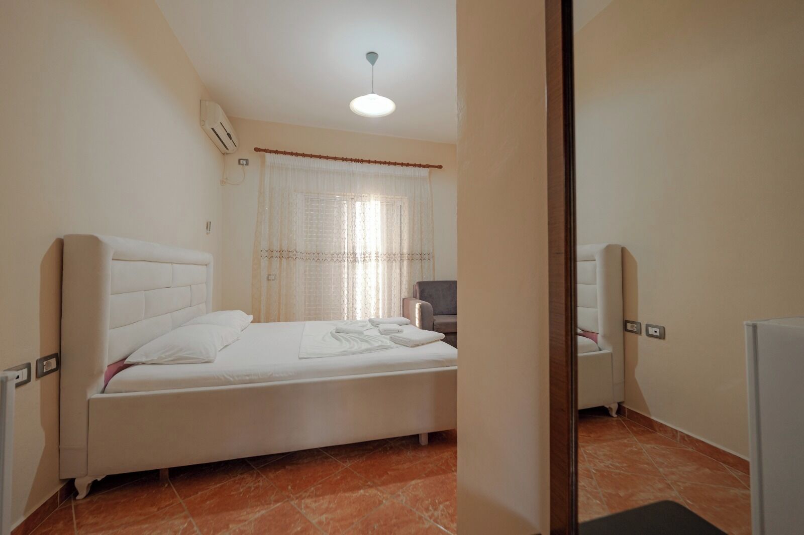 A bedroom with a bed, a chair, a desk, and a mirror.