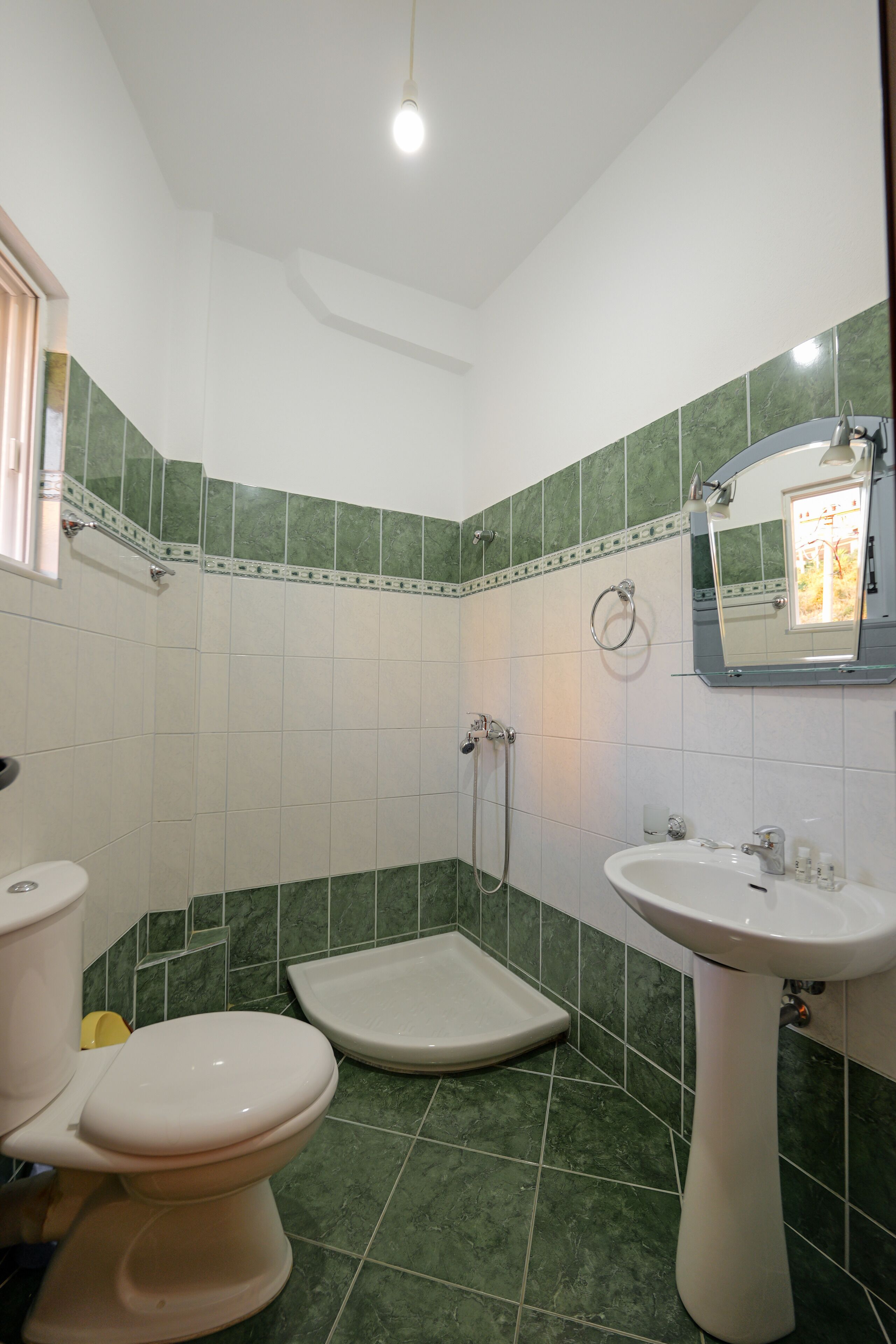 A bathroom with a toilet, bidet, and sink, featuring green and white tiles and a mirror above the sink.