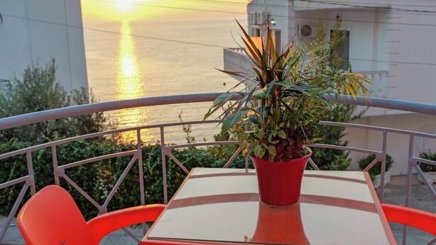 Un balcón con mesa y sillas, una planta en maceta y vista al atardecer sobre el mar.