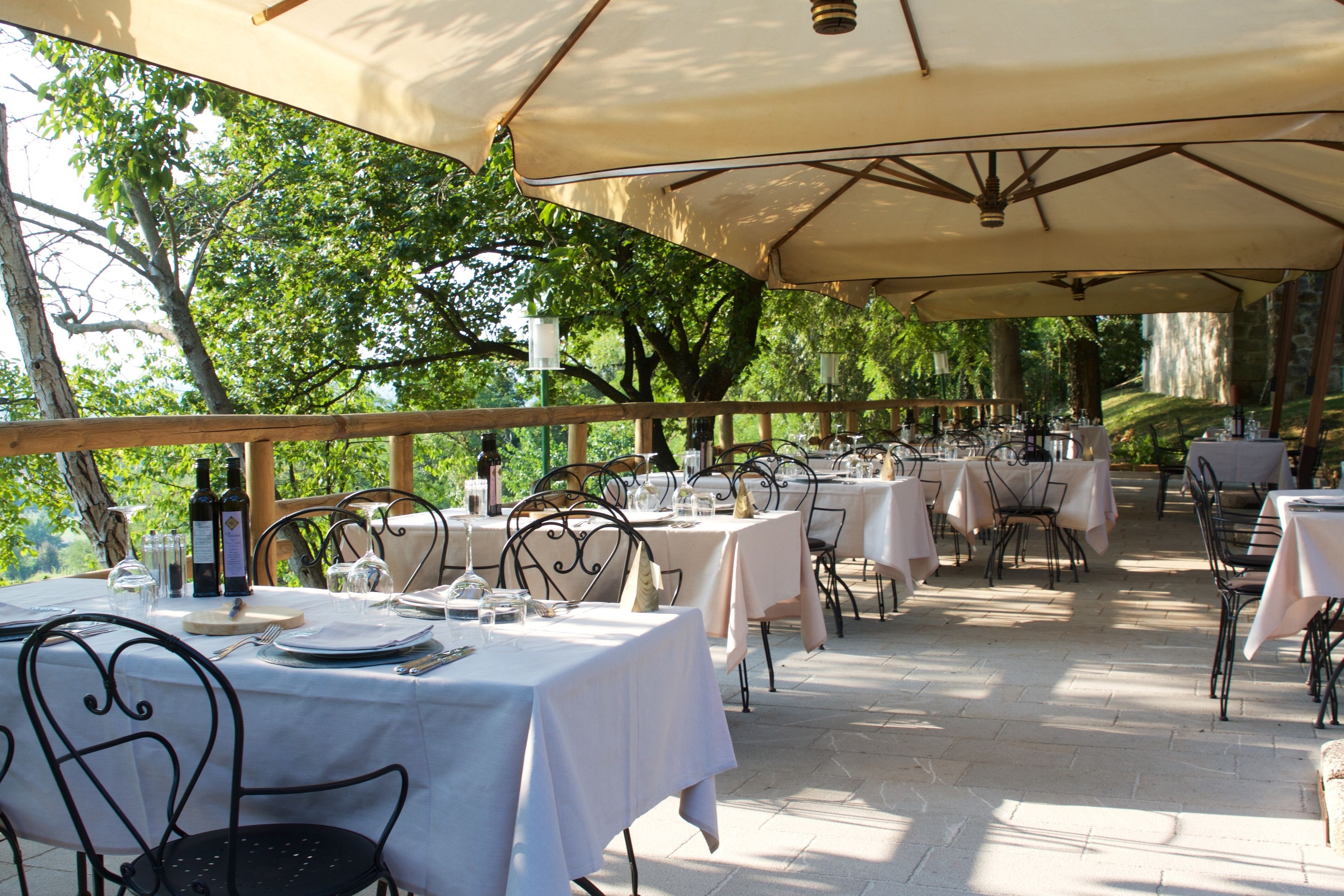 An outdoor dining area with tables covered by umbrellas, surrounded by trees.