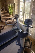 Un gimnasio en casa con cinta de correr, bicicleta estática y una escalera con planta en maceta.