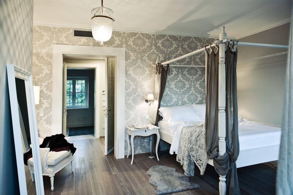 Une chambre à coucher avec un lit à baldaquin, une table de chevet, une chaise et une porte donnant sur une autre pièce.
