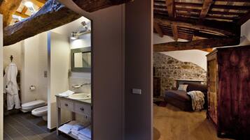 A rustic bathroom with a stone wall, wooden beams, a sink, and a toilet.