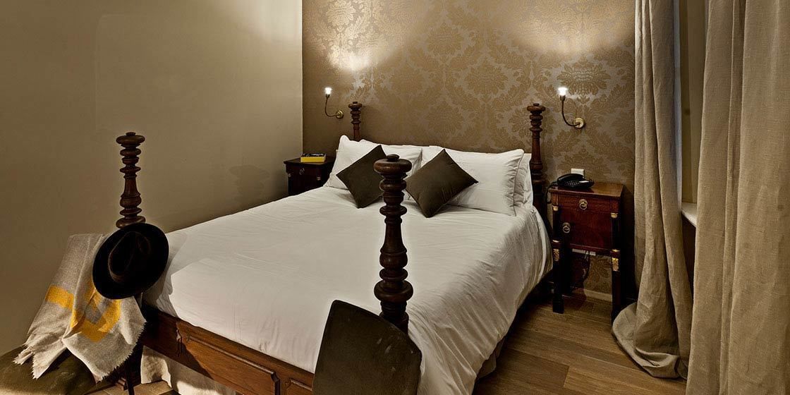 A neatly made bed with a wooden headboard, two bedside tables with lamps, and a curtain on the window.
