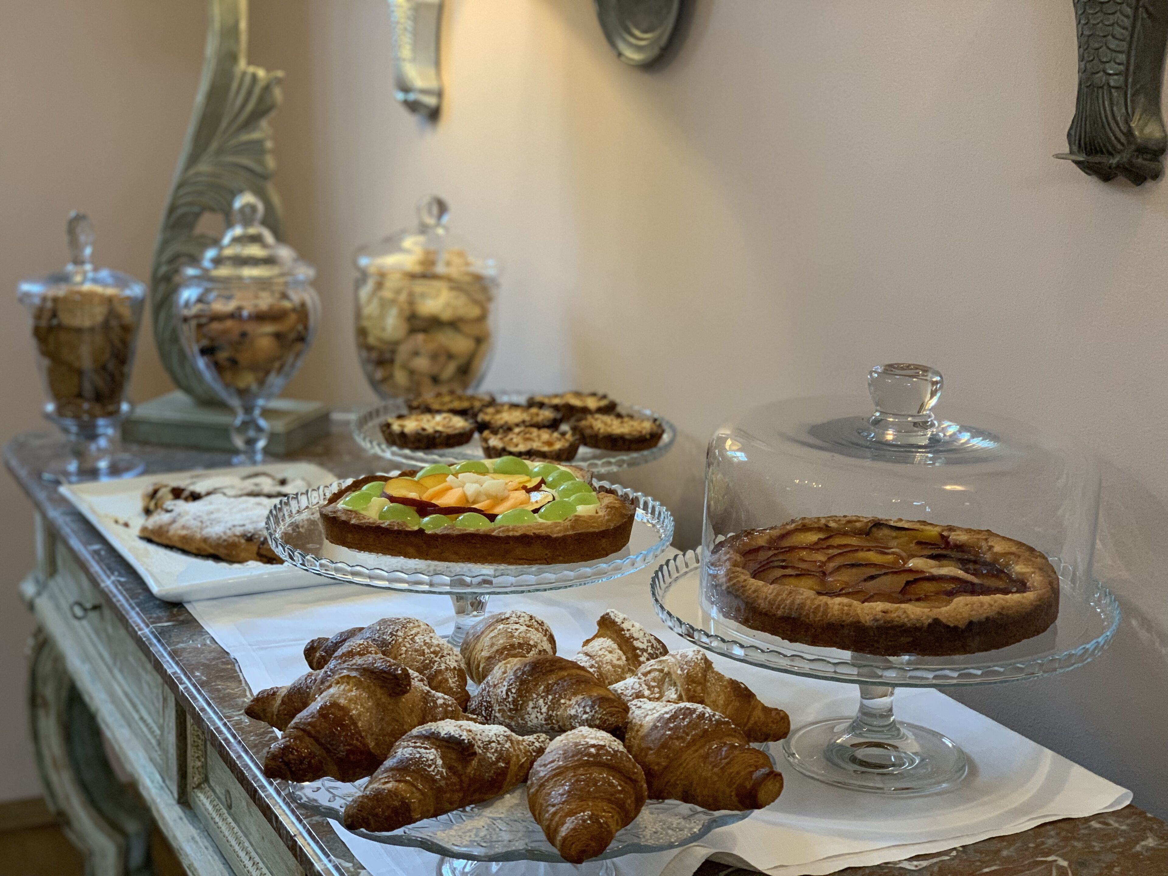 A buffet table with various pastries and desserts, including croissants and tarts, displayed on glass stands.