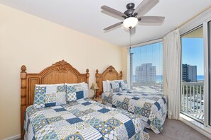 Quarto com duas camas, um ventilador de teto, mesa de cabeceira e janela com vista para a cidade.
