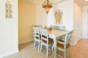 A dining area with a white table and chairs, a decorative mirror, and a hanging light fixture. - Open-concept, fully equipped condo w/private balcony! 🌴 (Destin)