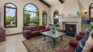 Un salón amplio con chimenea, sofás de cuero y ventanas grandes con vistas a un jardín.