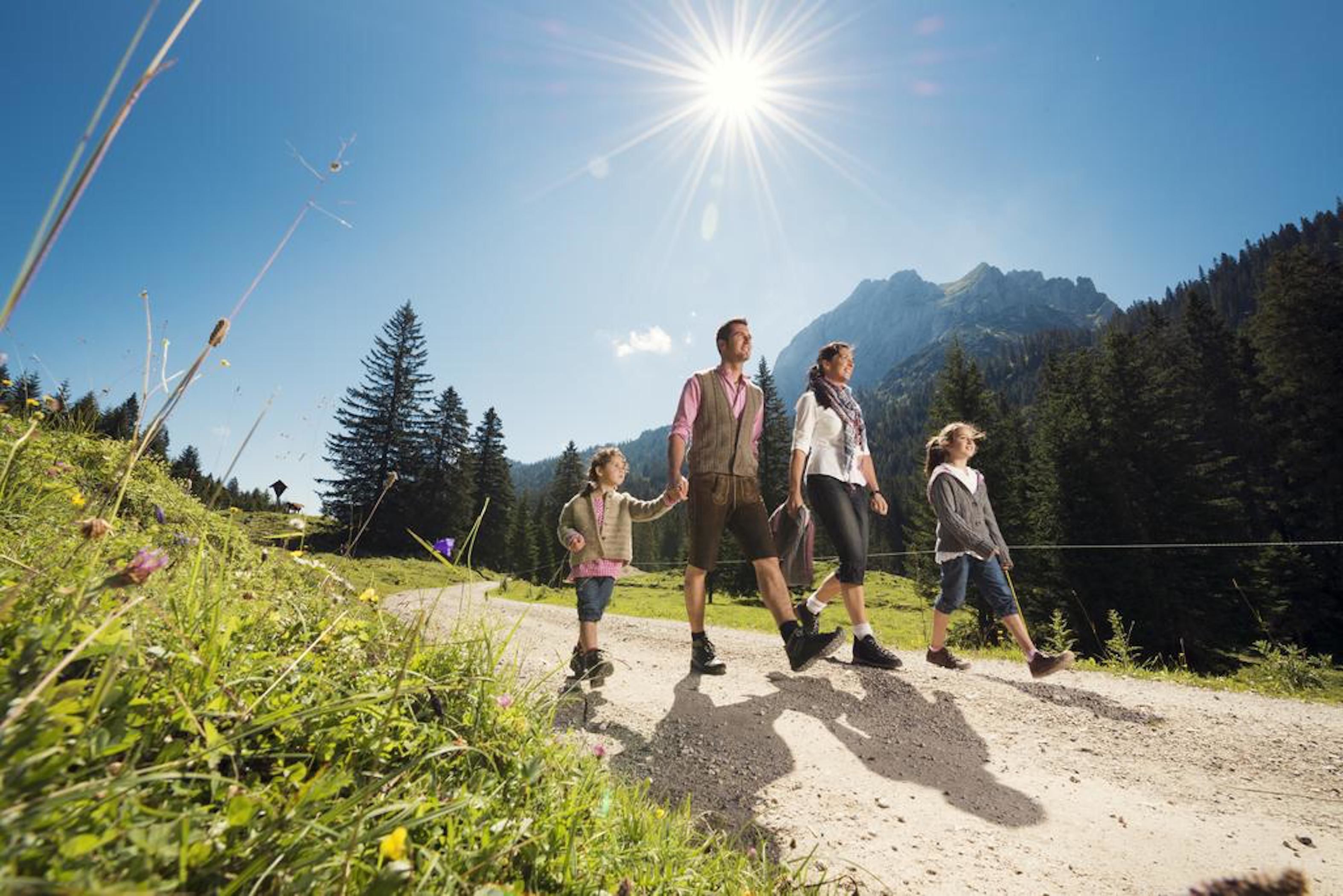Una familia caminando por un sendero de tierra con montañas al fondo y cielo despejado.