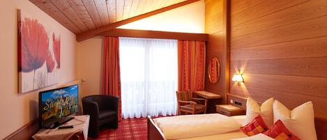 Habitación de hotel con techo de madera, cama con almohadas, escritorio con televisor, silla y ventana con cortinas.