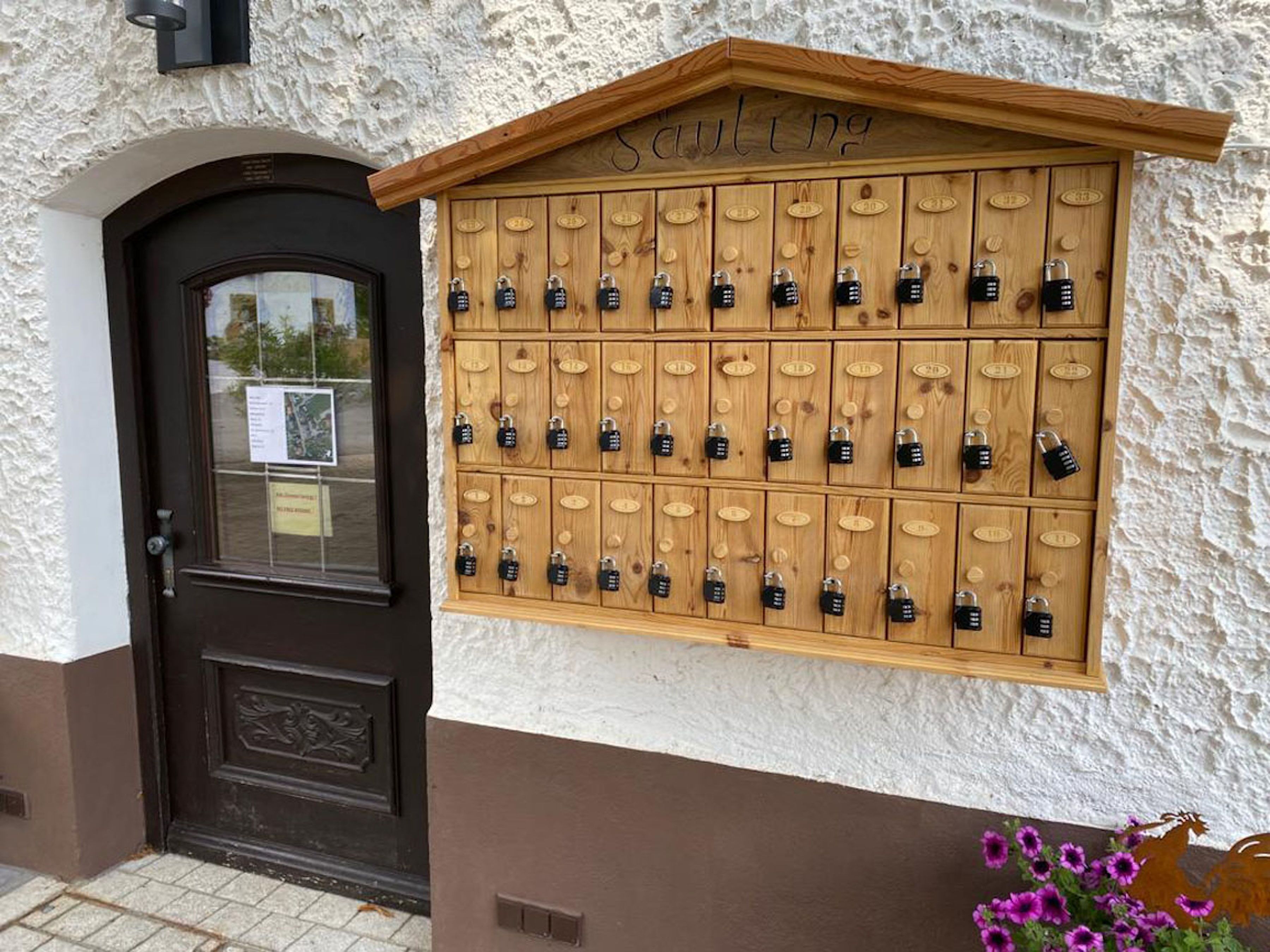 A wooden locker wall with multiple locks, a brown door, and a sign above it.