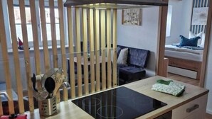 Cocina compacta con estufa, horno y pileta integrados. Se observa un separador de madera con listones verticales y una ventana con persianas.
