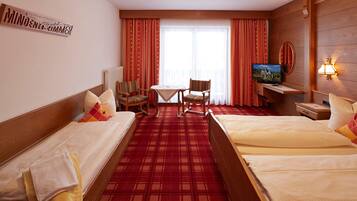 A hotel room with two beds, a small table, a chair, a TV, and a lamp.