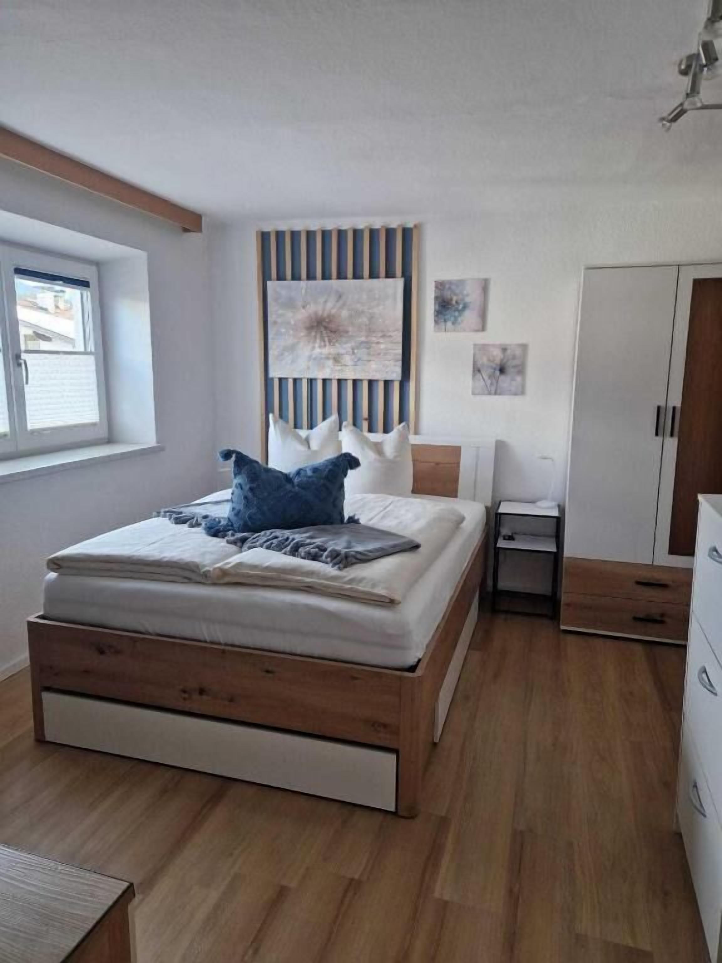 Een slaapkamer met een houten bed, nachtkastje, kledingkast en een raam.