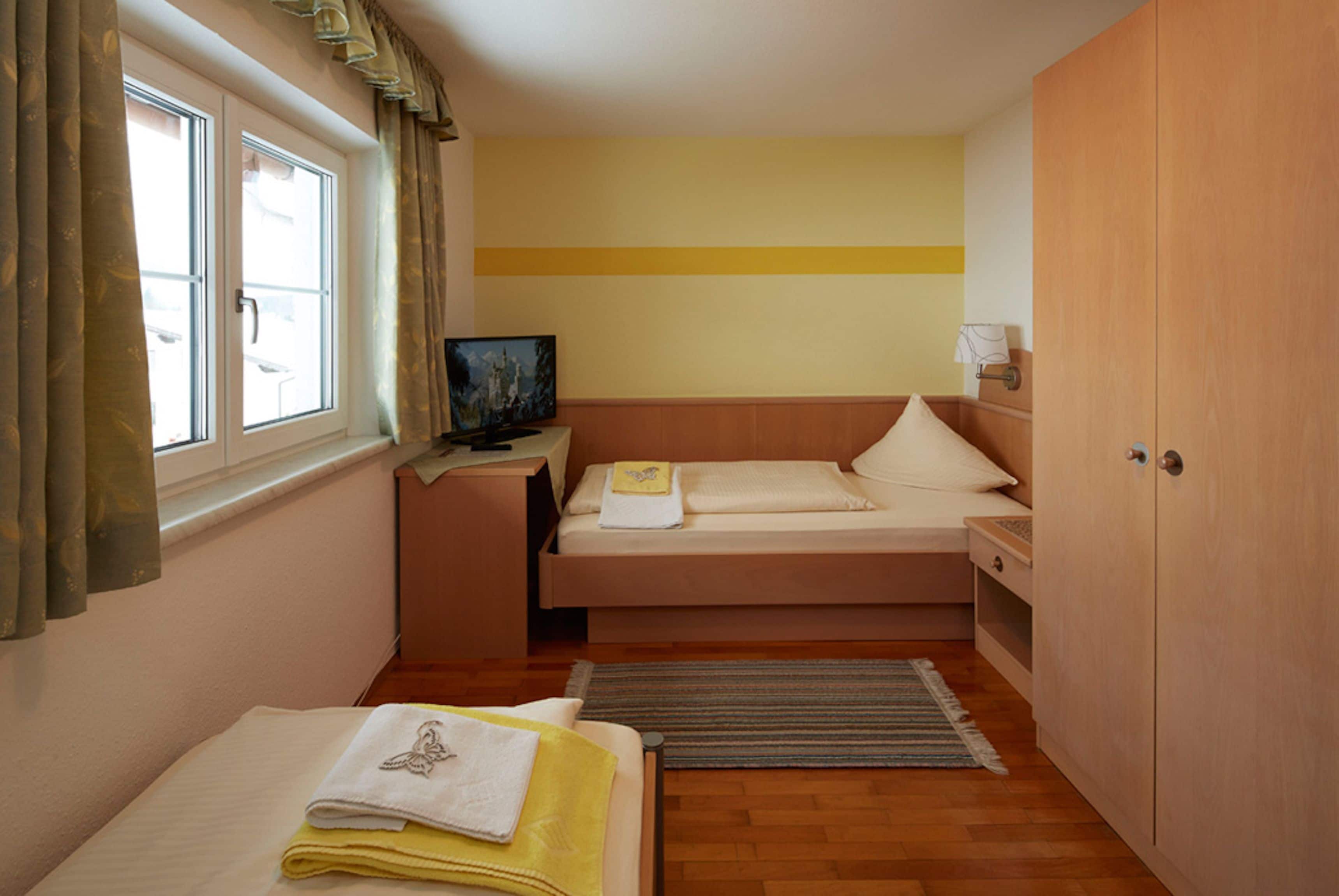 A compact bedroom with a single bed, a bedside table with a lamp, a television, and a wardrobe.