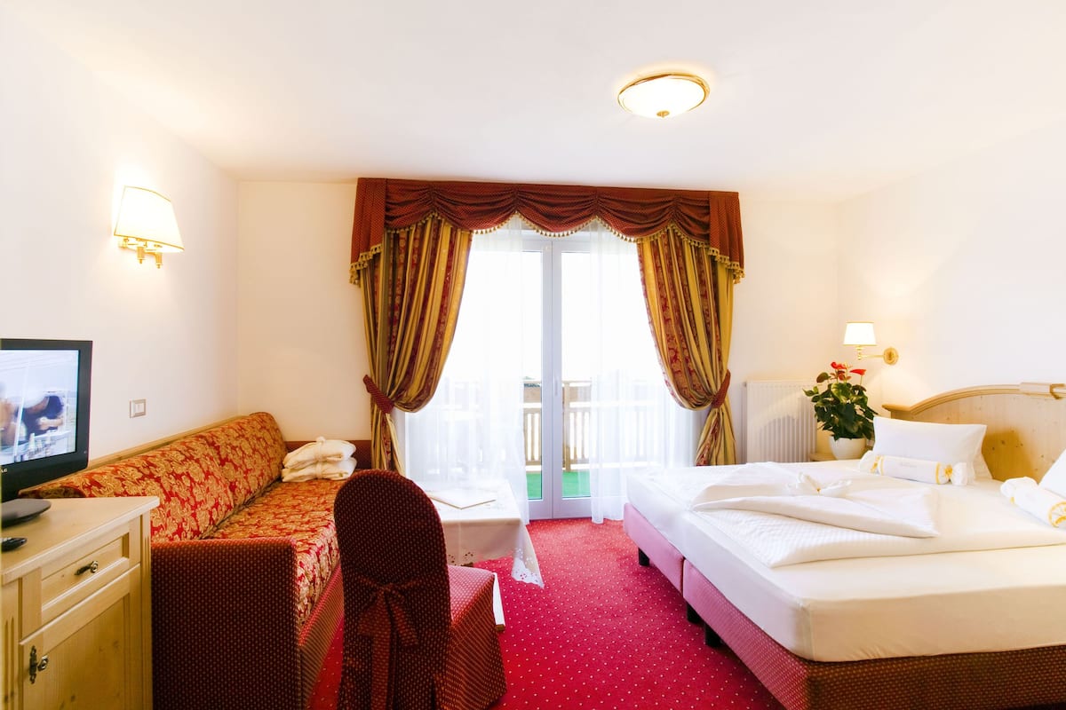 A hotel room with a sofa, a bed, a chair, a television, and a window with curtains.