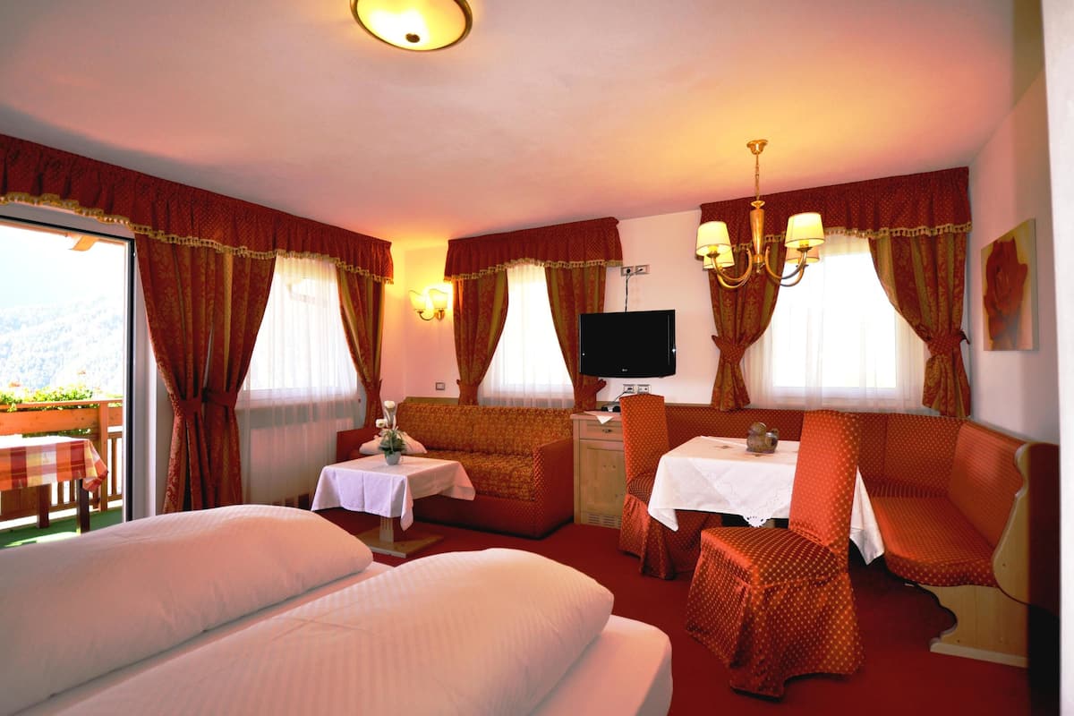 A hotel room with two beds, a dining table, a TV, and a balcony with a table and chairs.