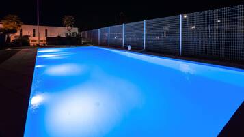 Una piscina con bordo illuminato di blu, circondata da una recinzione e un edificio sullo sfondo.