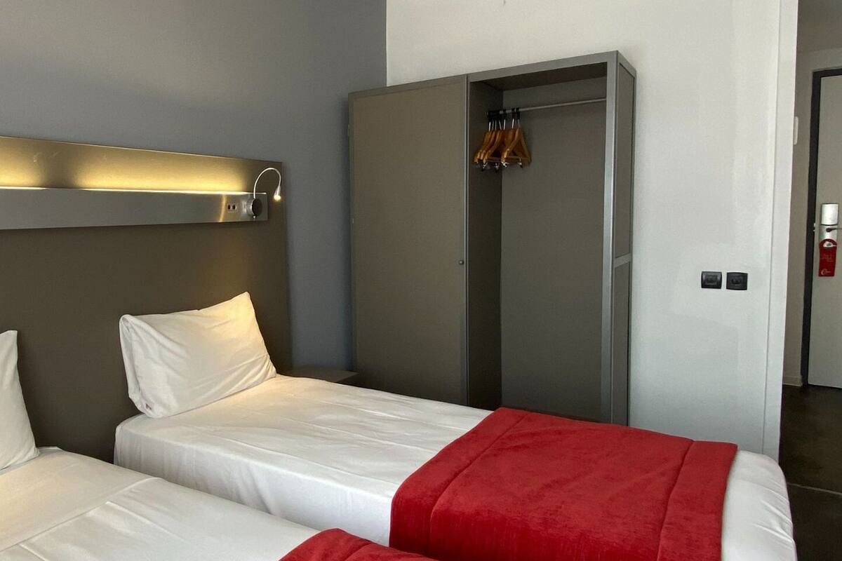 A hotel room with two beds, a wardrobe, and a mirror.