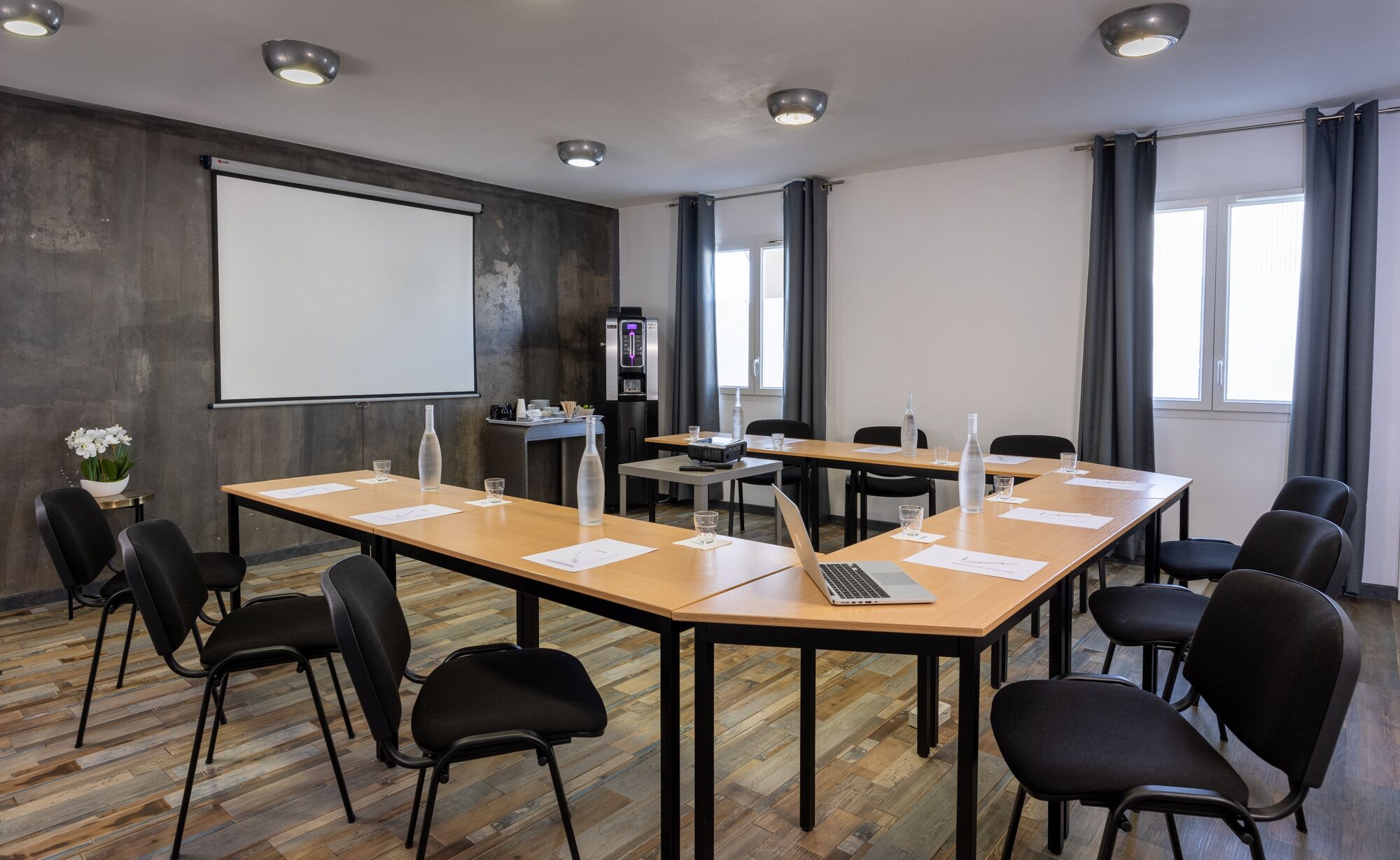A conference room with a large screen, wooden tables, black chairs, and a water dispenser.