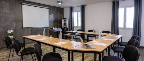 A conference room with a large screen, wooden tables, black chairs, and a water dispenser.