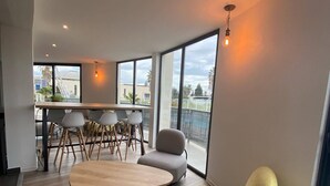 Una sala de estar moderna con una mesa de centro de madera, sillas grises y amarillas, y un balcón con ventanas amplias.