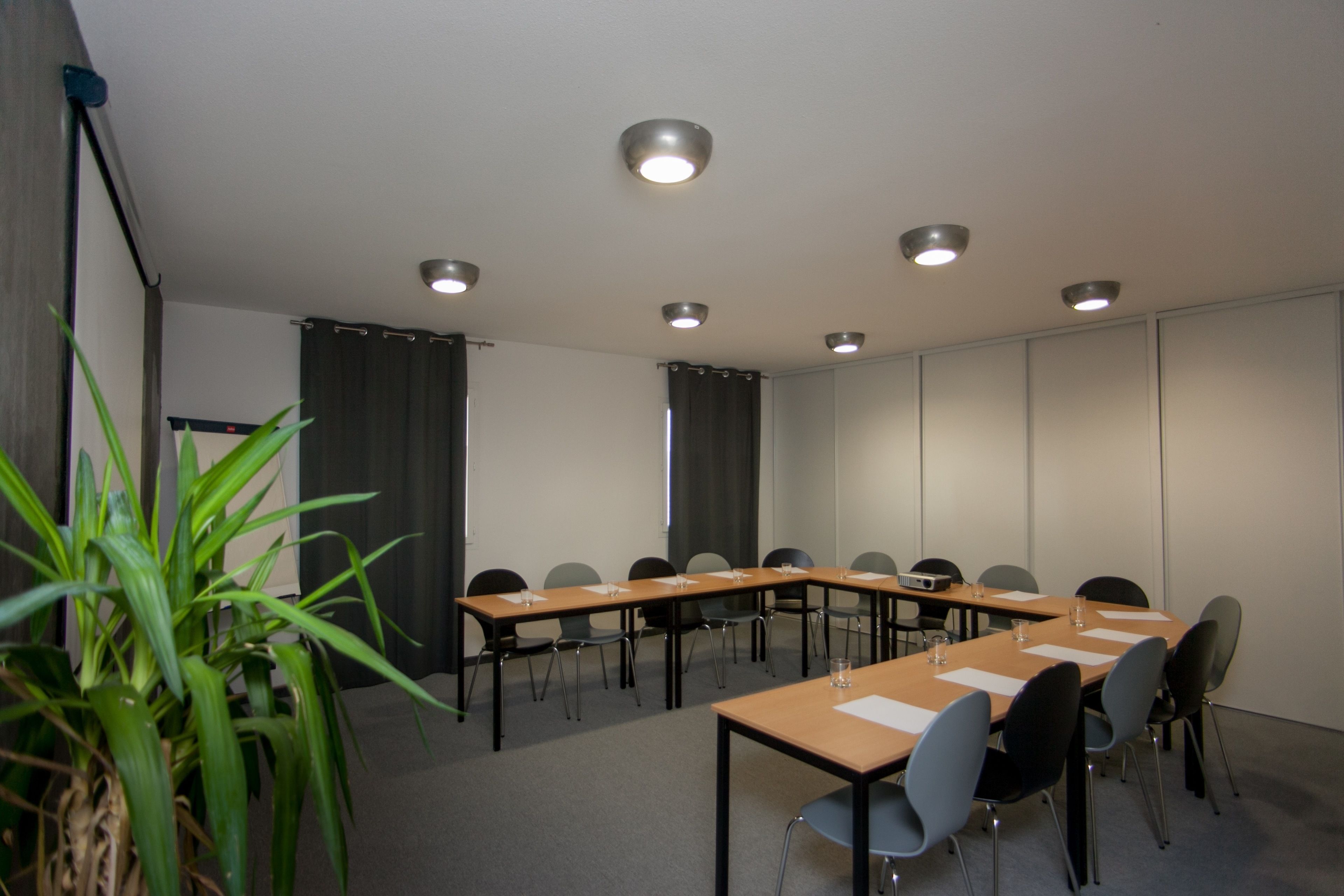 Une salle de conférence avec une longue table, des chaises et des luminaires au plafond.