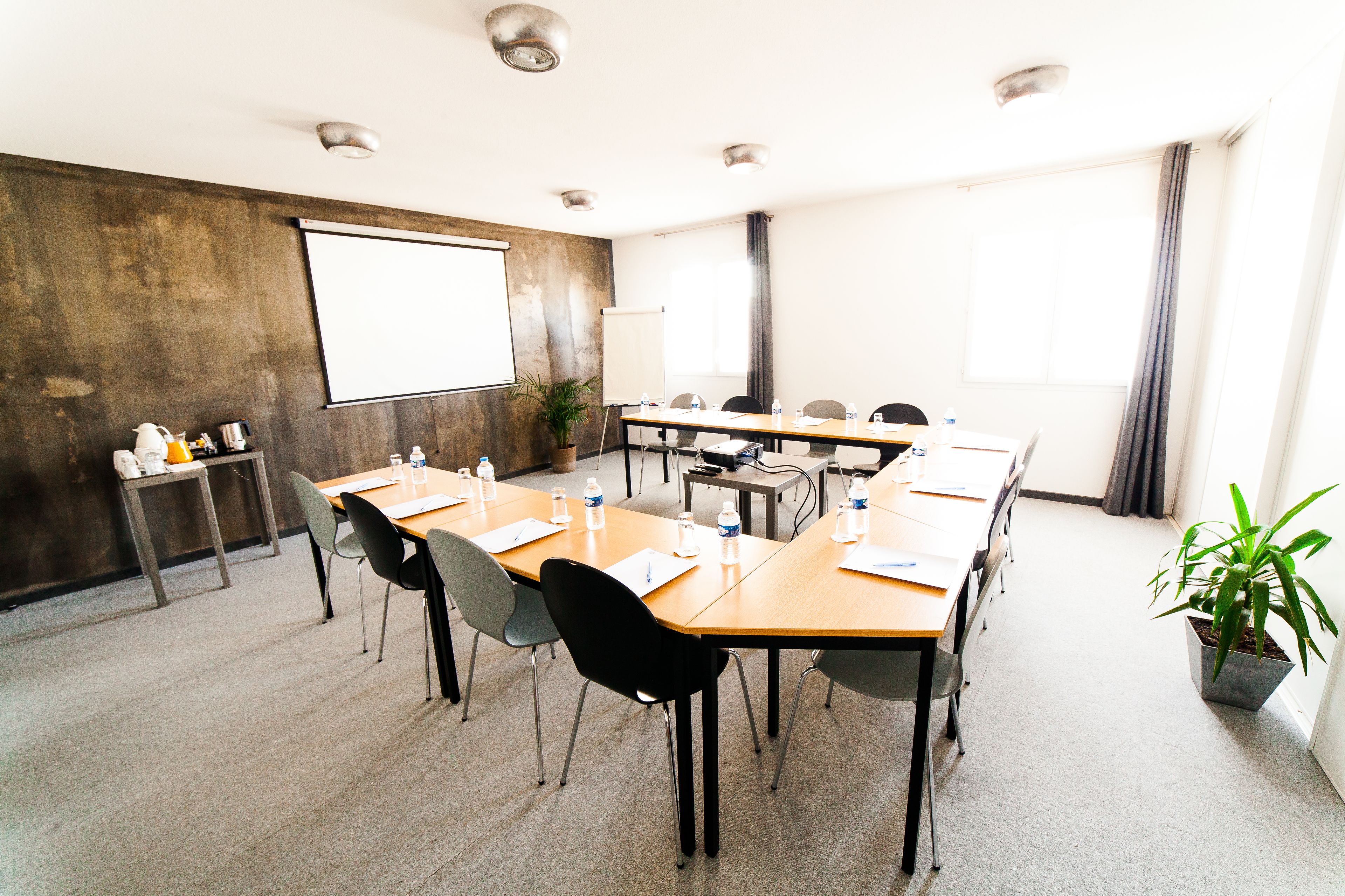 Una sala de conferències amb una taula gran, cadires, una pantalla de projector i una planta en test.
