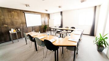 A conference room with a large table, chairs, a projector screen, and a potted plant.