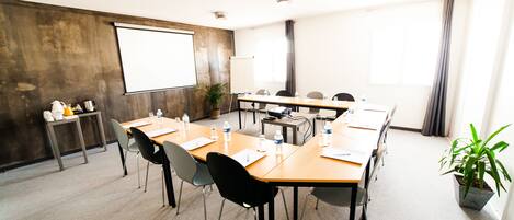 Ein Konferenzraum mit großem Tisch, Stühlen, einer Projektionsleinwand und einem Blumentopf.
