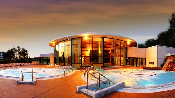 Un hotel moderno con zona de piscina circular, sillones de descanso y una cascada.
