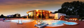 A modern hotel with a circular pool area, lounge chairs, and a waterfall feature. - The Originals City, Hôtel Les Dômes, Perpignan Sud (Saleilles)