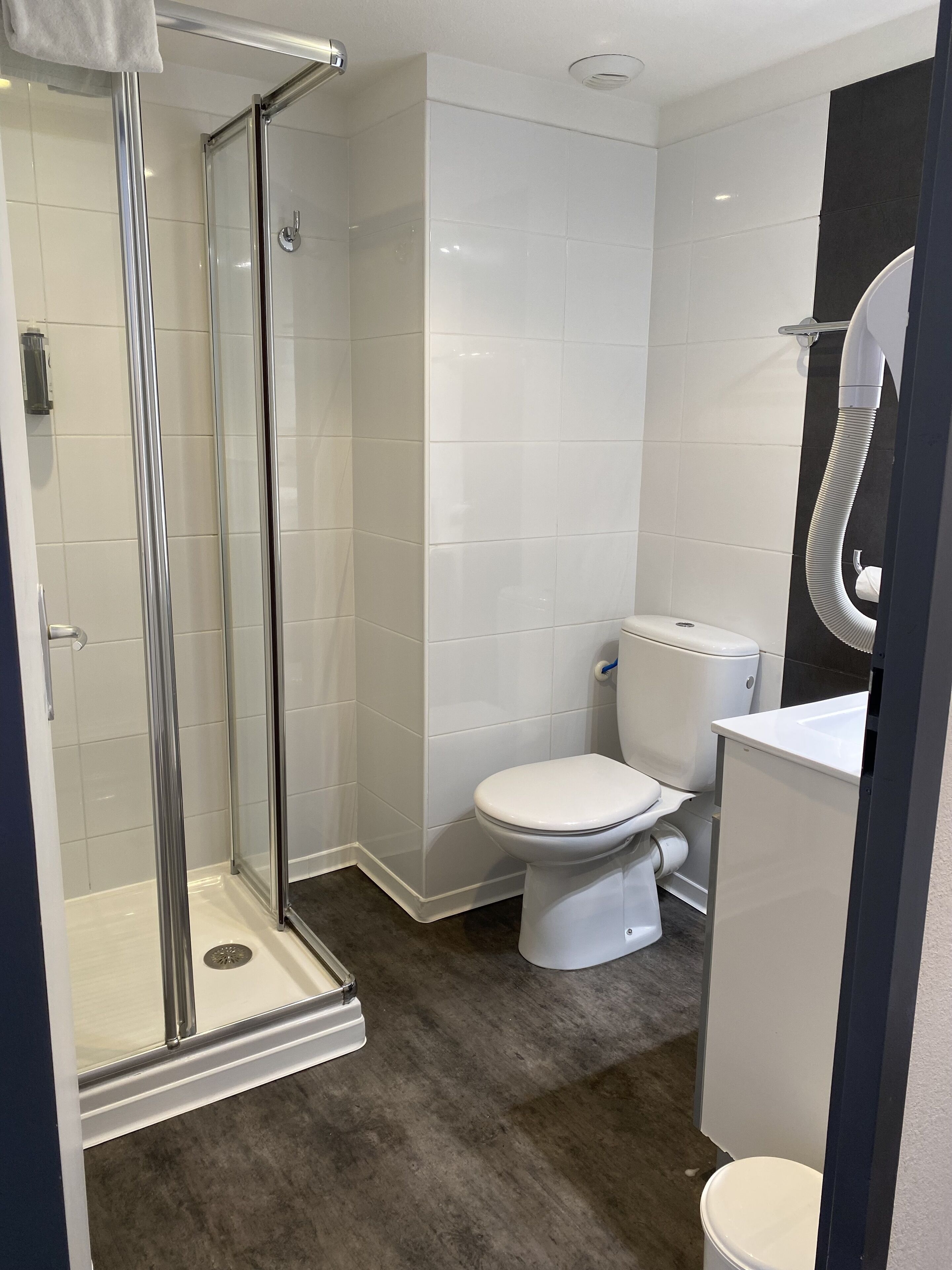 Un baño moderno con ducha de vidrio, inodoro blanco y lavamanos con espejo.